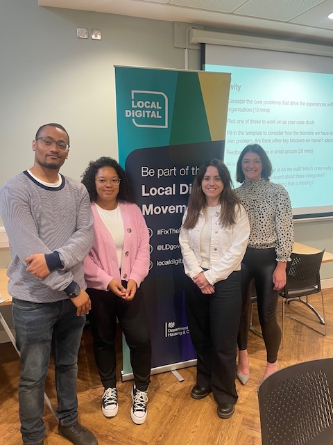 Leon (far left) and Eloise (second from left) presenting to colleagues at a Local Digital roundtable event in 2023. The presenters are standing in front of a display screen sharing information with the attendees.